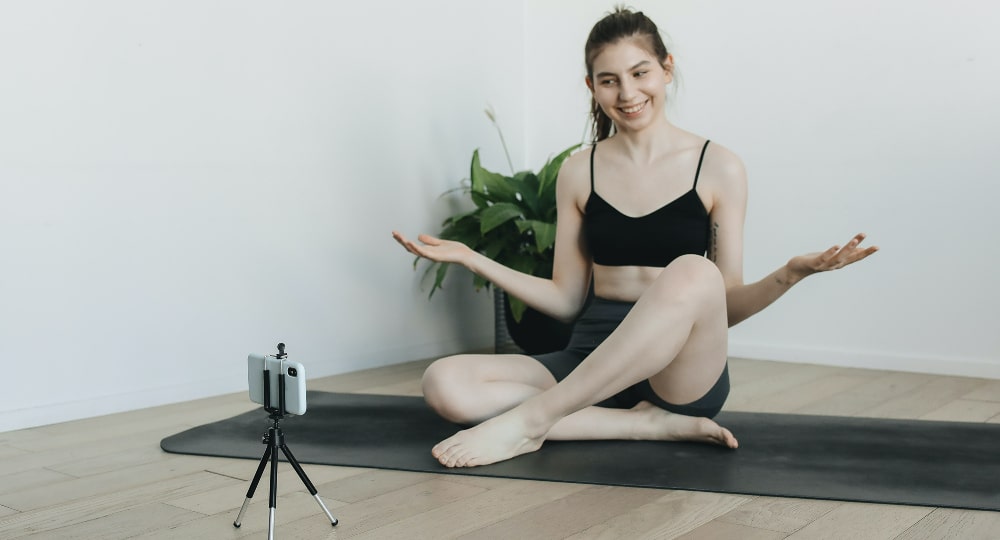 Ragazza sorridente fa lezione di home fitness in streaming con cellulare