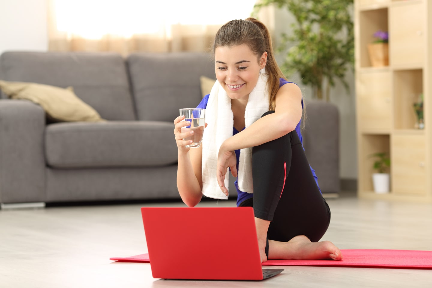 Giovane ragazza fa fitness davanti al laptop sorridendo con un bicchiere d'acqua
